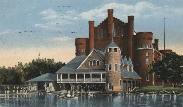 Boathouse on the University of Wisconsin-Madison campus. The Armory (Red Gym or Old Red) is behind the boathouse. In the left corner, a rowing ream is on the pier with a boat raised above their heads.