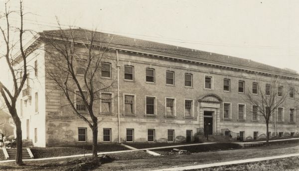 View of Bradley Memorial and University Infirmary on the University of Wisconsin-Madison campus. The building is now the School of Social Work. On the left near a flight of steps is a woman with children in baby carriages.