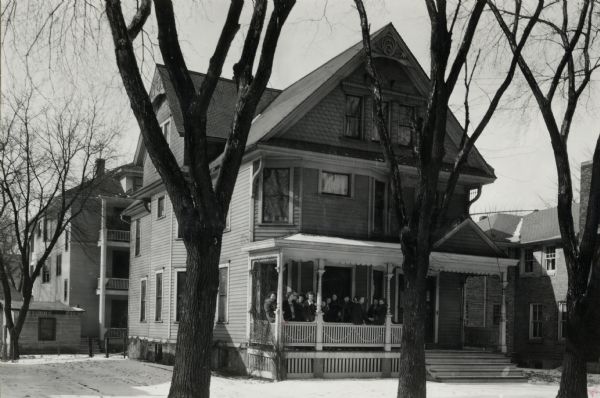 View from street of the porch of the house at the University of Wisconsin-Madison. A group of women are gathered on the fron porch. Snow covers the ground.