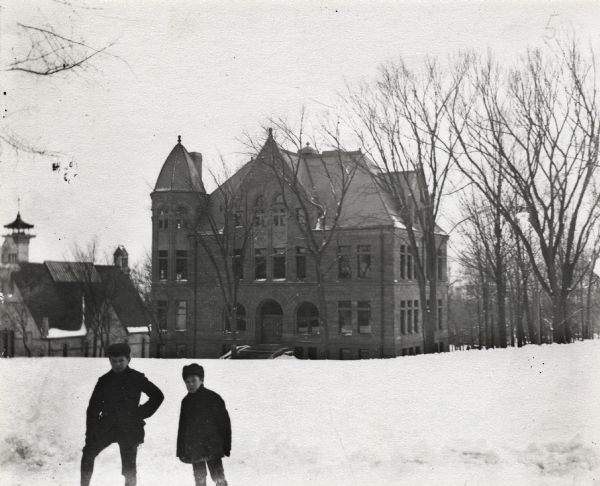 Two young children are standing on a snow-covered Bascom Hill, with the Law Building in the background on the University of Wisconsin-Madison campus.