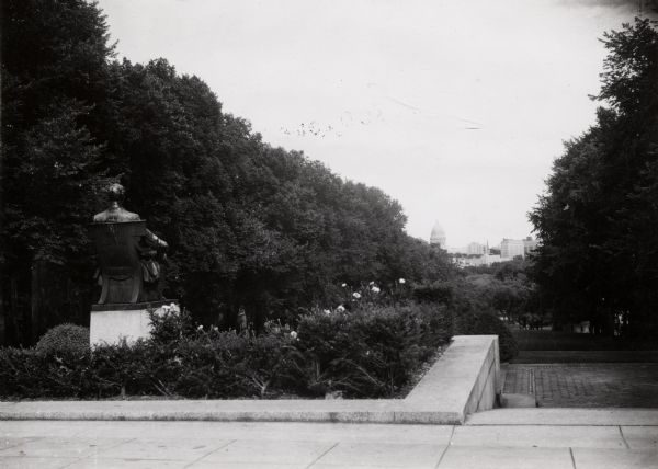 Rear view of Lincoln Monument on the University of Wisconsin-Madison campus. The monument is at the top of Bascom Hill, with flowering bushes and trees surrounding it. The Wisconsin State Capitol and several other buildings on the isthmus are in the far distance.