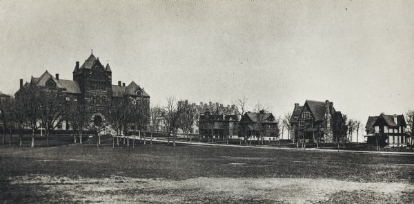 View across open area with trees of the lower campus at the University of Wisconsin-Madison. Science Hall is on the left, and four dwellings are along Langdon Street with Lake Mendota in the background.