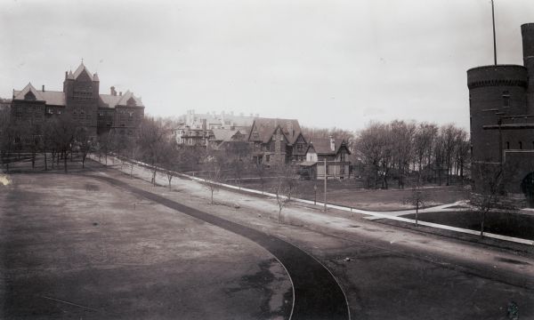 Elevated view across open space with an oval track, looking towards Science Hall at the end of Langdon Street on the University of Wisconsin-Madison campus. Houses are along the shoreline of Lake Mendota across the street, and the Red Gym (Old Red) is on the right.