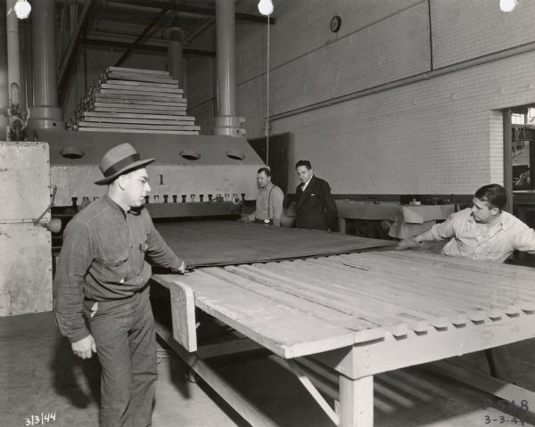 Consolidated Paper executive Jim Plzak (in the suit), watches as workers pull laminate from the Number #1 press at the Consolidated Paper Company.  The laminate was used in the manufacture of lightweight gliders for the military during World War II.