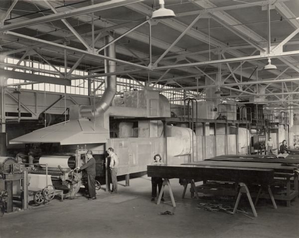 Interior view of the Consolidated Paper Company factory showing the large treater used in the manufacture of glider parts during World War II.  Ralph Turner, in the light sweater, watches as plastic impregnated paper emerges from the dry end of the treater.