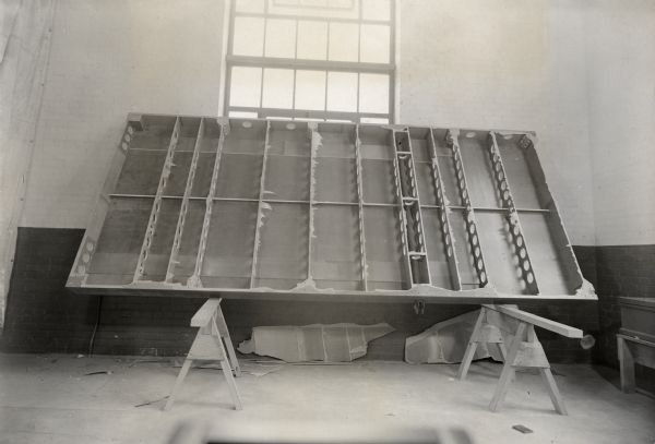 Prototype glider floor turned on its side on two saw horses to be photographed.  The glider was being developed by the Plastics Division of the Consolidated Paper Company as part of its war effort.