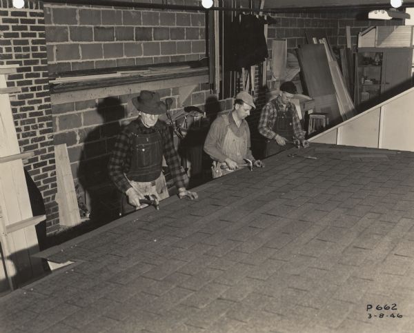 Employees of the Plastics Division of Consolidated Paper Company shingle a roof in a factory.  The roof was then taken to the building site for final assembly.
