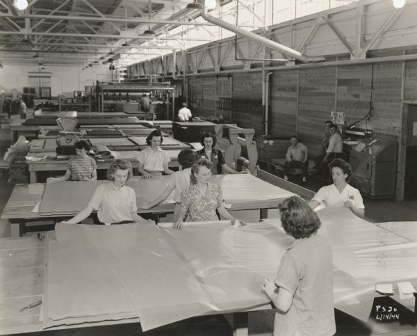 Women employees of the Plastics Division of Consolidated Paper Company performing an early layup operation, a part of the process whereby the company made paper-based plastic laminates for the military during World War II.