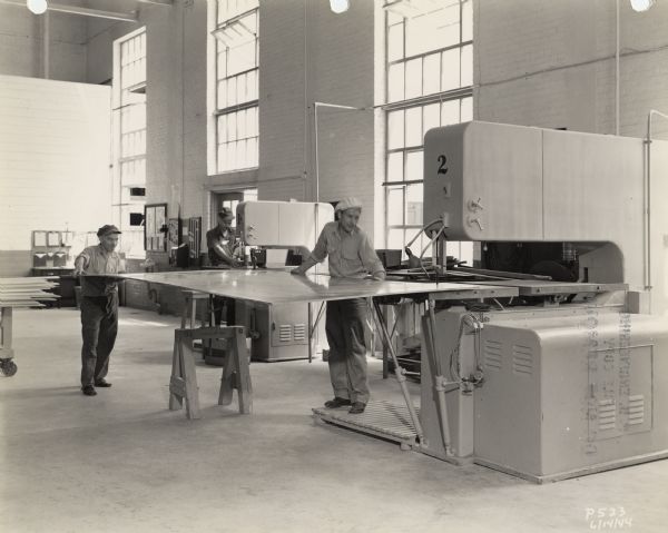 Employees of the Plastics Division of Consolidated Paper Company demonstrating the use of two pieces of equipment used in cutting the paper-based laminate produced by the company during World War II.