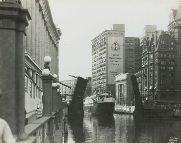 An open drawbridge with a boat crossing below. The First National Bank is in the background.