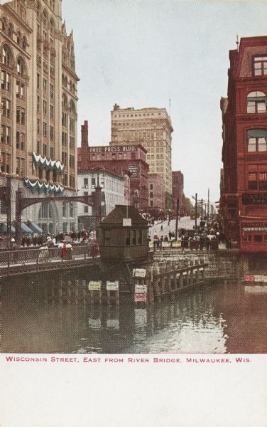 View across river toward Wisconsin Street and the River Bridge. Caption reads: "Wisconsin Street, East from River Bridge, Milwaukee, Wis."
