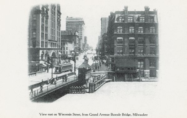 Slightly elevated view of Wisconsin Street, with the bridge on the left. Caption reads: "View east on Wisconsin Street, from Grand Avenue Buscule Bridge, Milwaukee."