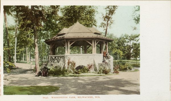 Visitors around a gazebo or pavilion in Washington Park. A group of people are posing on the curved stairway on the right side of the pavilion. Caption reads: "Washington Park, Milwaukee, Wis."