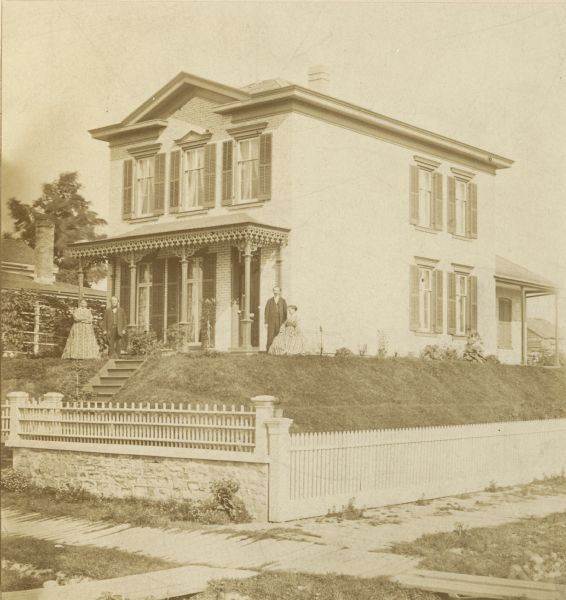 Exterior view of the Emil Wallber house with four people standing near the entrance. Wallber was the mayor of Milwaukee from 1884-1888. The location of the house was probably 604 Galena Street at its intersection with Sixth Avenue. This house was reported to be the first brick house to be moved in the city.