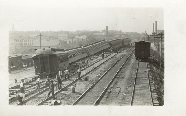 Elevated view of train cars that have fallen off the railroad tracks, with men working nearby.