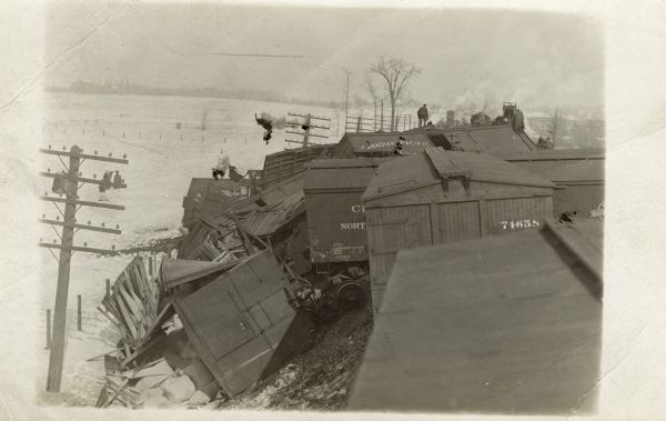 Elevated view of railroad cars that have fallen off the railroad tracks. Two men are crawling on top of the toppled railroad cars.