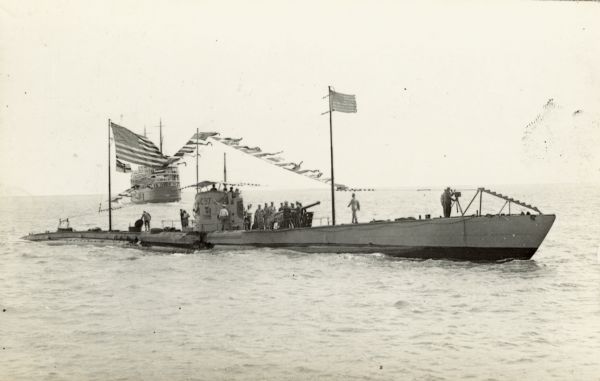 Captured German submarine, possibly the U-C97, with men on deck. United States flags are flying and several men are gathered on top of the submarine. Another ship can be seen in the background.