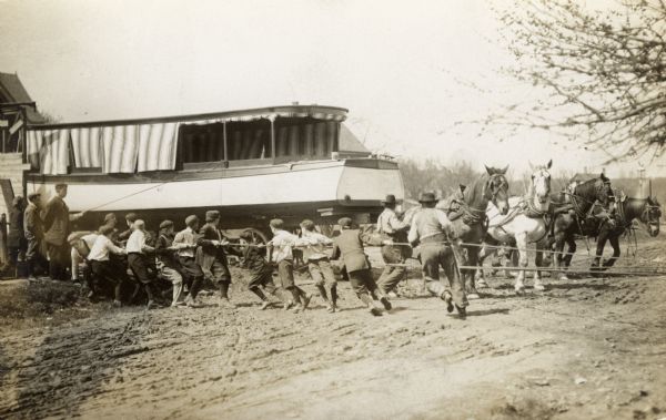 Boys, men, and horses hauling a boat with ropes.