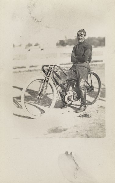 A man is posed outdoors on an early motorcycle.