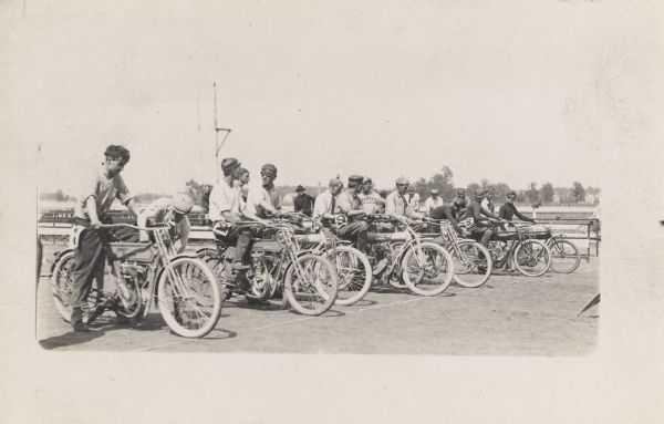 A group of men are lined up on motorcycles on a track preparing to race.