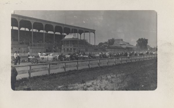A long row of cars is lined up across the track on display. On the left side is the "Blitzen Benz".  A grandstand is in the background.
