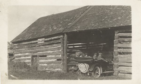 The Milwaukee Journal Pathfinder parked inside a log barn. Four people (two women, two men) are sitting in the car. The Pathfinder sign is on the back of the automobile.