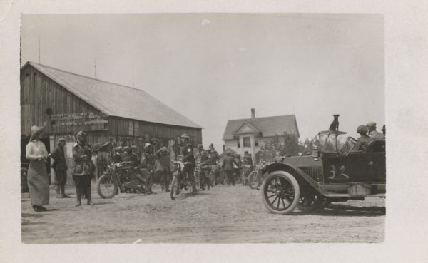 A group of motorcyclists and enthusiasts gathering outside of a barn.
