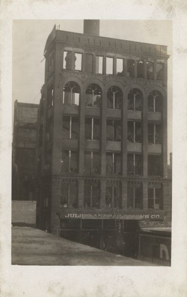 Elevated view of the empty, burnt remnants of a building still partially standing. On the bottom, leaning against the second floor, is a ladder coming up from the street.