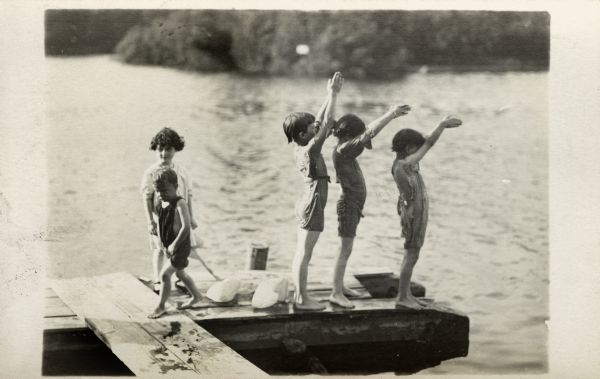 A group of children, possibly J. Robert Taylor's sons and daughters, playing on a pier. Three of the children are lined up in diving poses getting ready to dive into the lake.