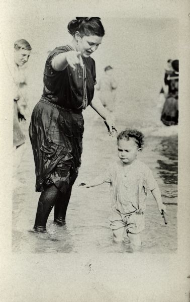 Woman and child standing in a lake in shallow water. Other people are standing in the water behind them.