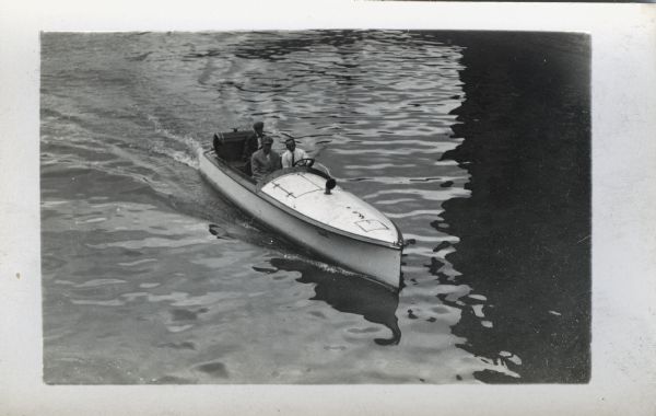 Elevated view of three men riding in a long, narrow motorboat on a lake.