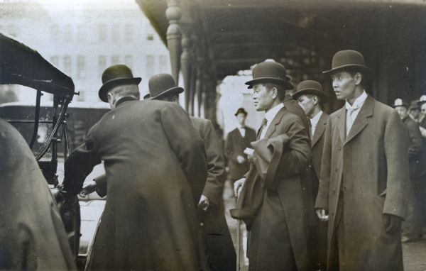 Asian men on the street, entering a car.
