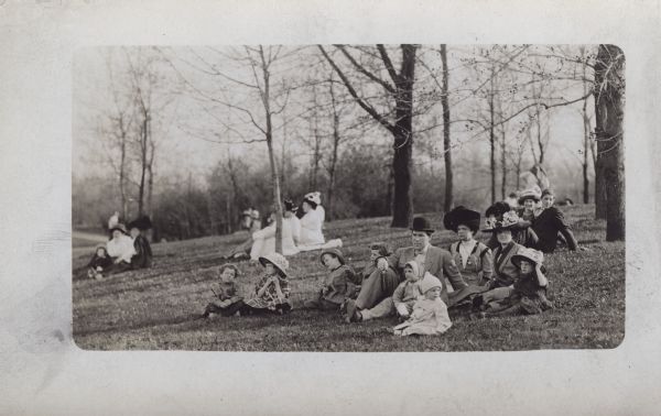 A group is sitting on the lawn at Washington Park. Louis Oto Stauff is wearing the bowler hat. The women behind him are identified as Ella Augusta Reinhardt Stuaff, Louis' wife, and Alma Reinhardt Taylor, J. Robert Taylor's wife. The children are identified as Roy Reinhardt Stauff (on Louis' right), Ruth May Stauff (on Louis' lap) Glenn and Clyde Stauff, Ellen Taylor (to the left), Donna Taylor (next to her mother), and Frederick Taylor.