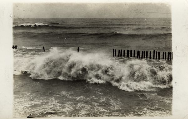 Elevated view of Lake Michigan, showing waves crashing near a row of pilings.