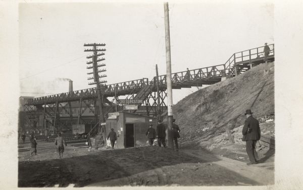 Men walking near the railroad Crossing Store. Above the store is a bridge providing a walkway over the railroad tracks.