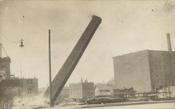 Demolition of a smokestack. The stack is falling into a pile of rubble not far from the road.