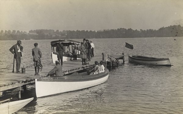 Three boats next to a pier. The one on the end of the pier is the <i>Intrepid</i>, the one in the foreground, in which three people are sitting, is the <i>Elizabeth</I>. Another boat on the right at the end of the pier is unidentified.