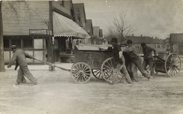 Men pushing and pulling two carts, one with a barrel, around a street corner.