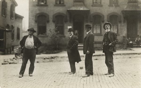 Four men standing on a paved city street in front of a house.
