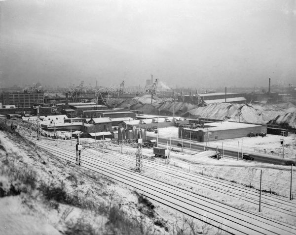 Elevated view of the Milwaukee Electric Rapid Transit at 20-23rd Streets and St. Paul, looking southeast from a hillside. Snow is on the ground, the buildings, and the large piles of coal or coke in the distance.