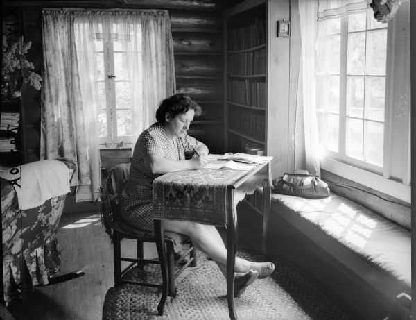 Woman sitting at a writing desk at Estella's. She is facing a bright window which has a window seat.
