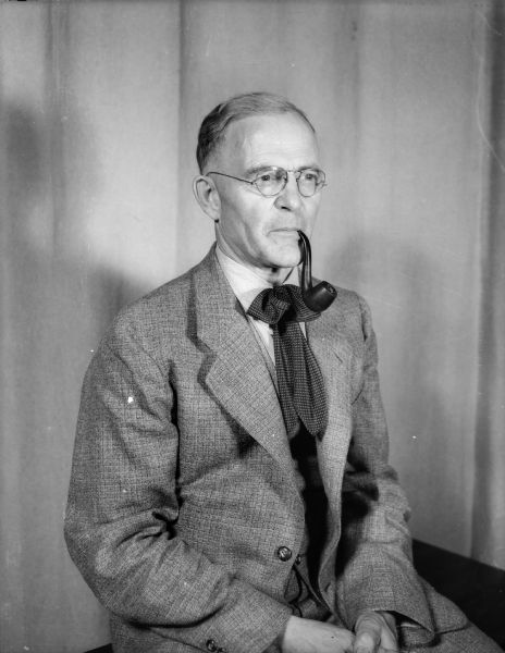 Studio portrait of J. Robert Taylor with a pipe in his mouth.