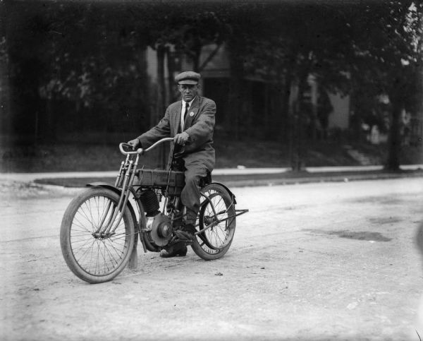 J. Robert Taylor is posing on his motorcycle in the middle of a neighborhood street.
