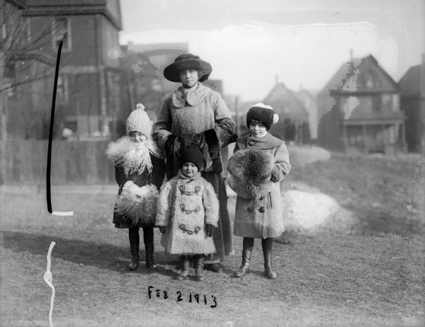Alma Reinhardt Taylor with her three children, Donna, Ellen, and Fred, standing outdoors in the winter weather. All but the smallest child have furry hand muffs. Snow is on the ground behind them.