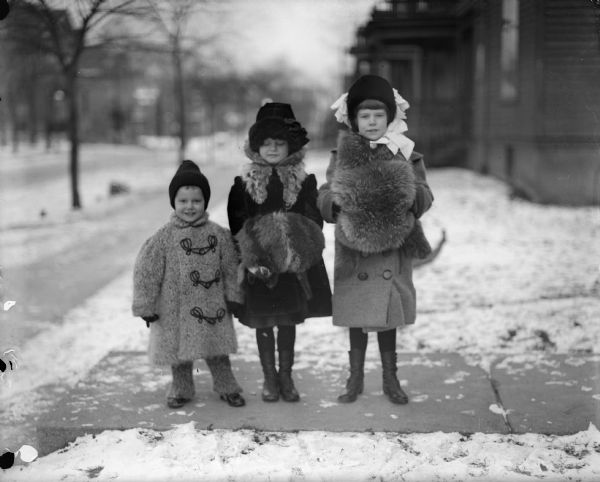 Frederick, Donna, and Ellen Taylor dressed in winter clothes outside in winter time. The two girls are wearing muffs to warm their hands.