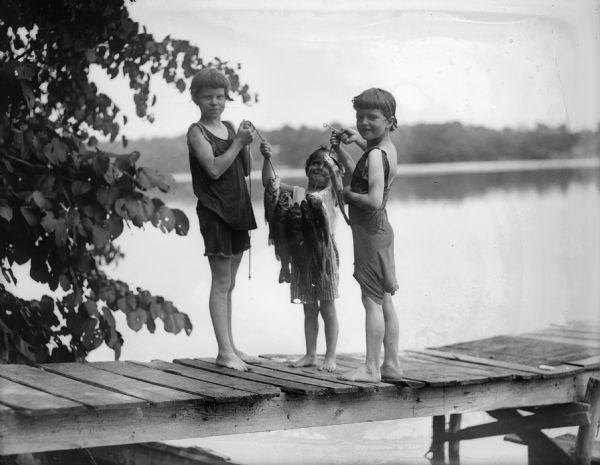 Ellen, Donna and Fred Taylor standing on the dock of a lake with a string of fish held up between them.
