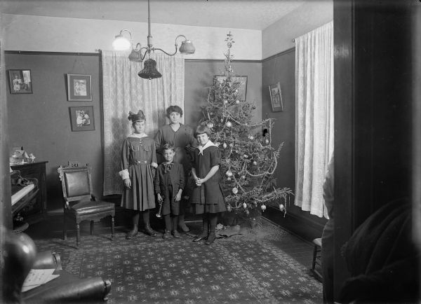 Family posed with Christmas tree in living room.  Identified from left as Donna Taylor Adams, Alma Reinhardt Taylor, Ellen Taylor Higgins, and Fred Taylor (front).