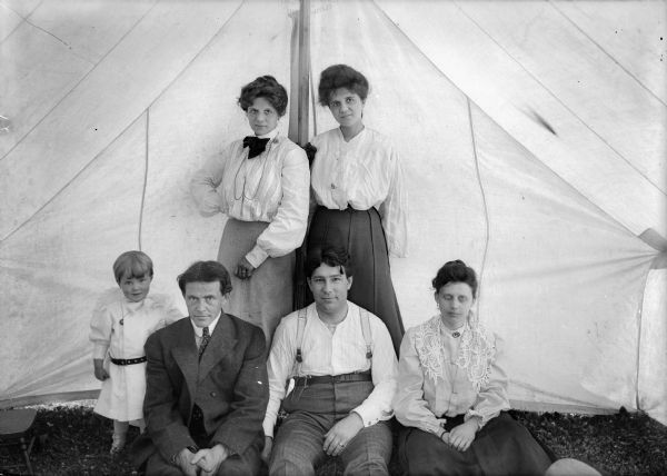 Family posed in front of a camping tent.  Identified in front row: Ellen Taylor Higgins, J. Robert Taylor, Louis Otto Stauff, and an unknown woman.  Back row:  Alma Reinhardt Taylor, Ella Reinhardt Stauff.