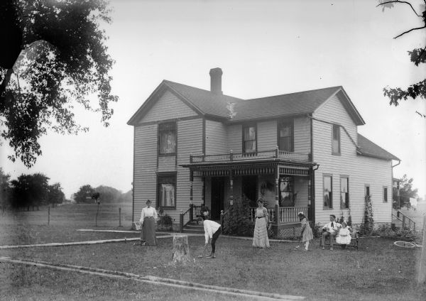 Family playing croquet in the front yard of a rural home.