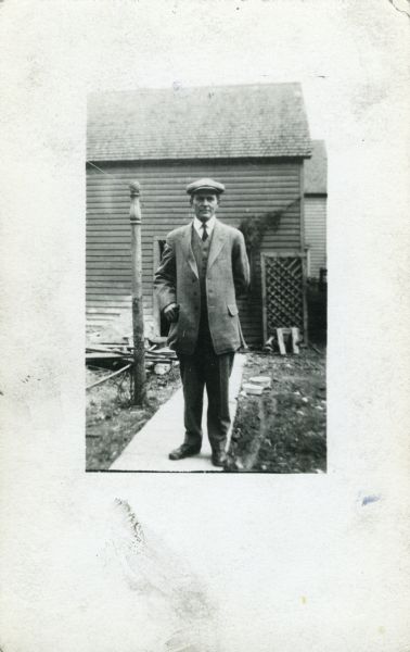 J. Robert Taylor standing on a walkway in a yard with a wooden building in the background.